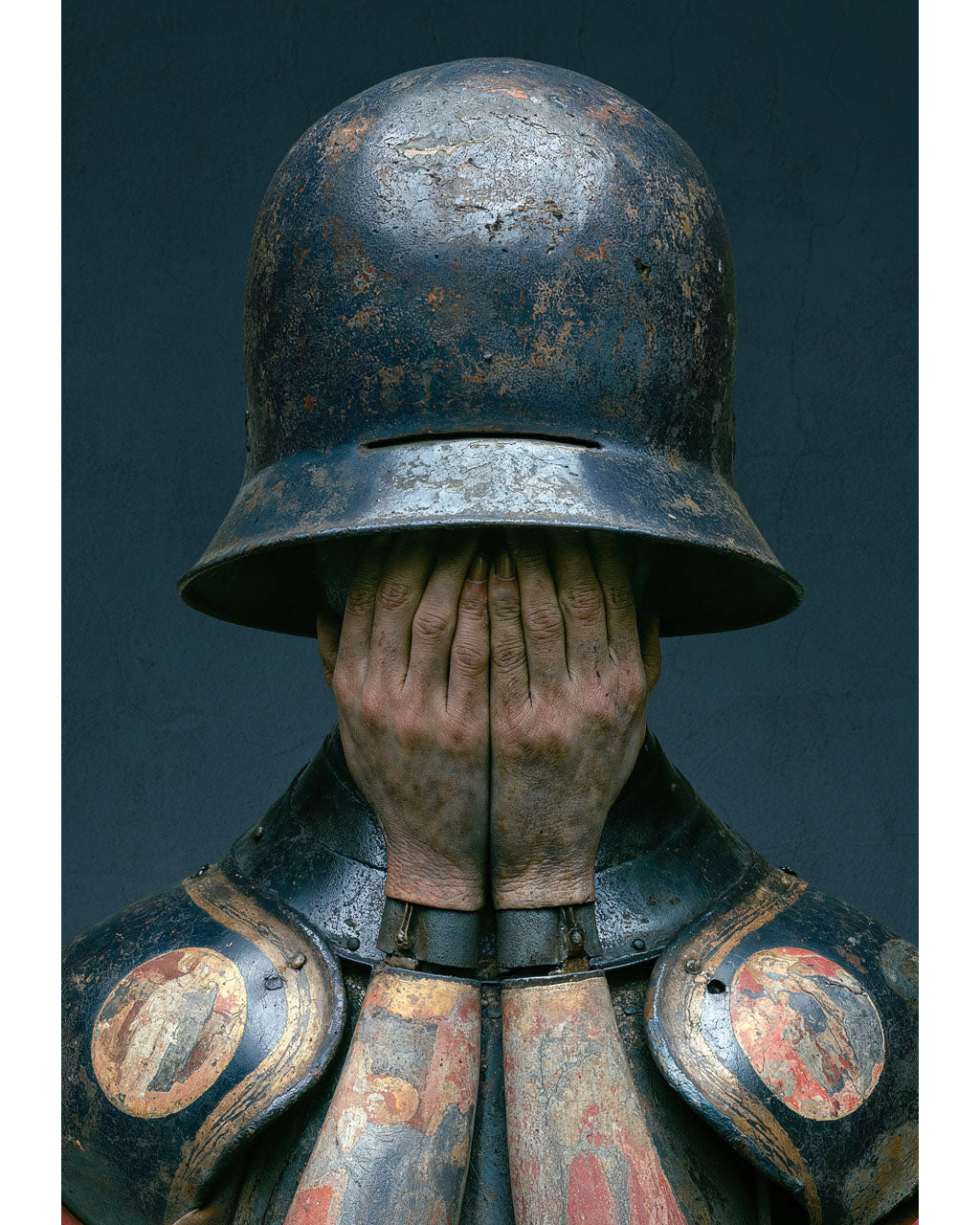 Surreal armoured figure covering their face beneath a weathered helmet