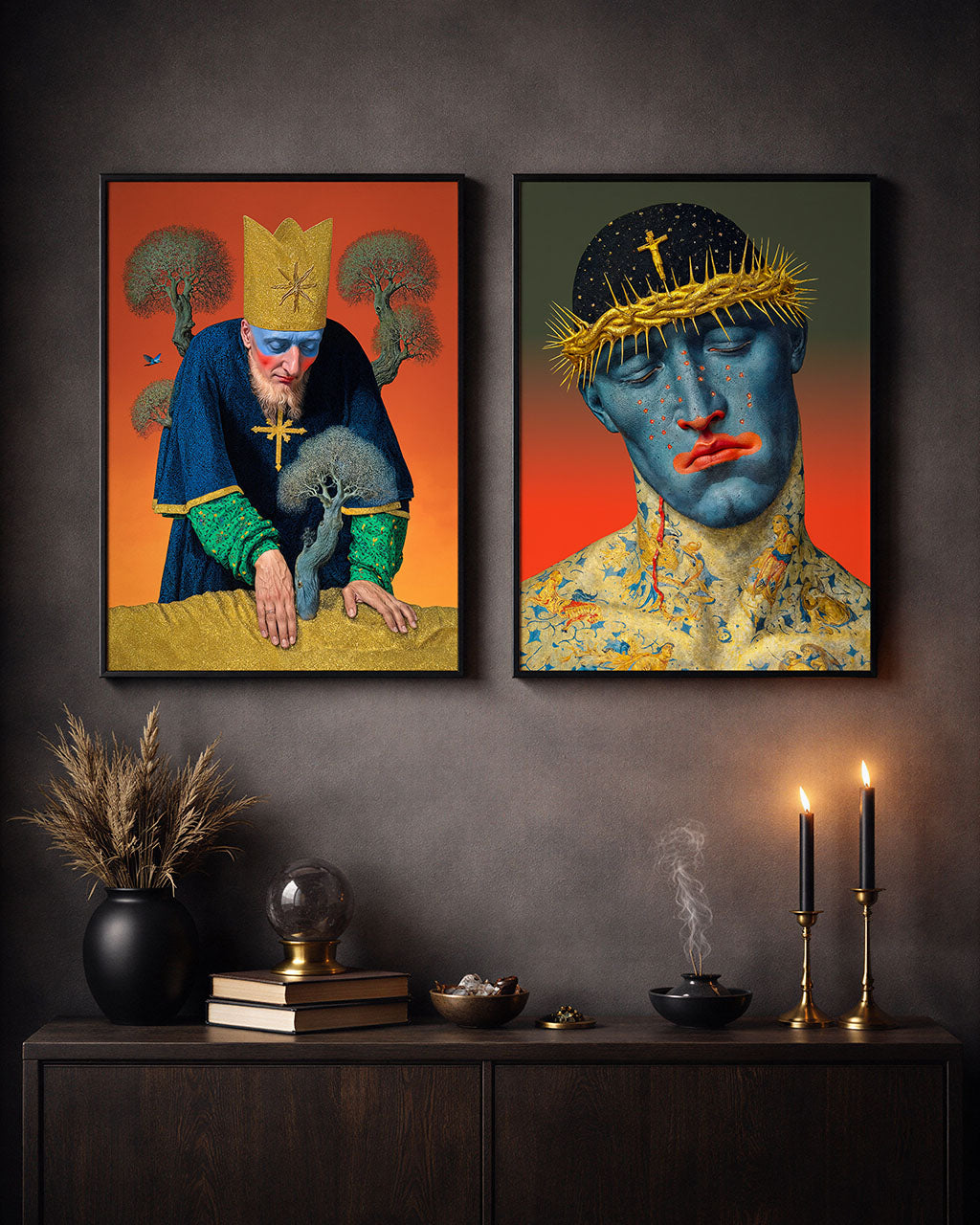 Two framed surreal portrait posters with intricate details displayed above a dark wooden console table with candles, books and decorative objects in a moody interior.