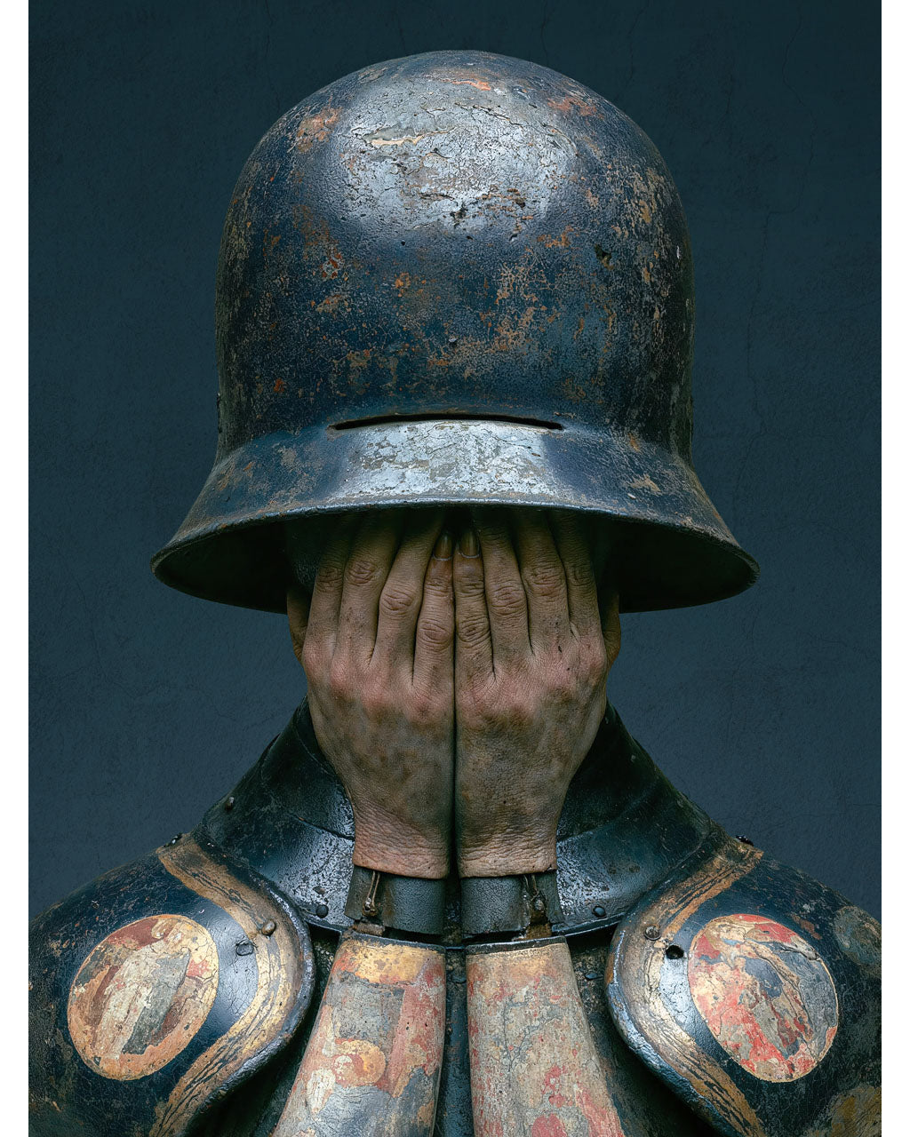 Surreal armoured figure covering their face beneath a weathered helmet
