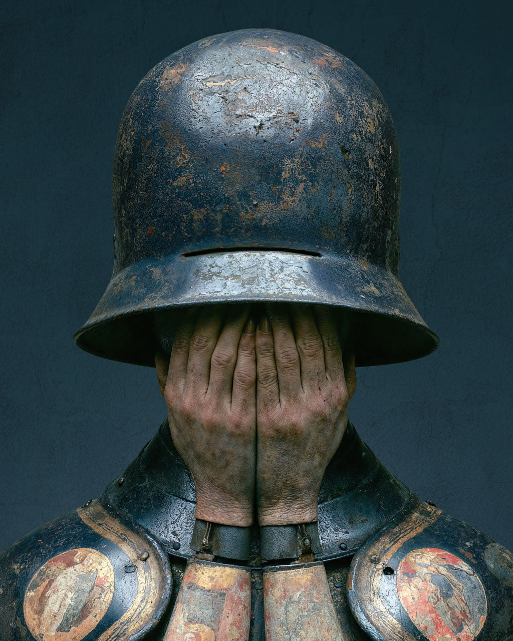 Surreal armoured figure covering their face beneath a weathered helmet
