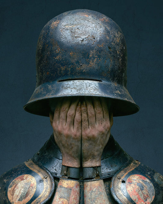 Surreal armoured figure covering their face beneath a weathered helmet