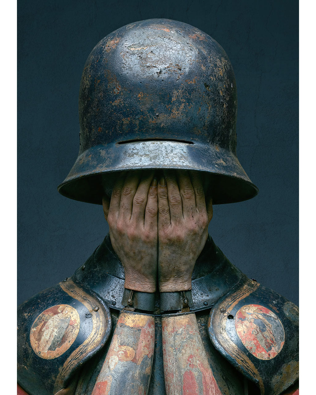 Surreal armoured figure covering their face beneath a weathered helmet